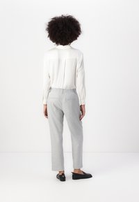 Une personne portant une chemise blanche à manches longues et un pantalon gris clair avec une taille élastique et deux poches arrière, vue de dos.
