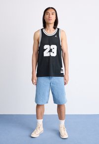Zwarte mesh basketbaltop met witte nummer 23, gecombineerd met lichtblauwe spijkerbroekshorts en beige hoge sneakers. Minimalistisch ontwerp.