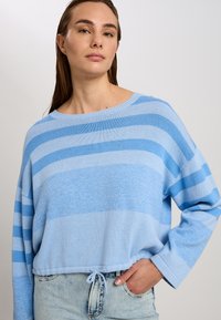 Hellblau gestreifter Strickpullover mit weitem Halsausschnitt und langen Ärmeln, ausgestattet mit einem Kordelzugsaum und unterschiedlichen Blautönen in horizontalen Streifen.