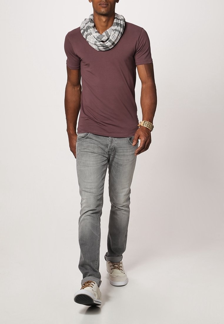 Homme marchant portant un t-shirt grenat, un jean gris, des baskets blanches, une écharpe rayée noir et blanc, et un bracelet marron.