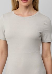 Robe grise clair à manches courtes avec un col rond, fabriquée dans un tissu lisse et légèrement scintillant, présentant un bodice ajusté et une jupe évasée.