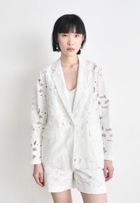 White lace blazer with floral patterns, featuring a single-button closure and two front pockets, paired with matching shorts.