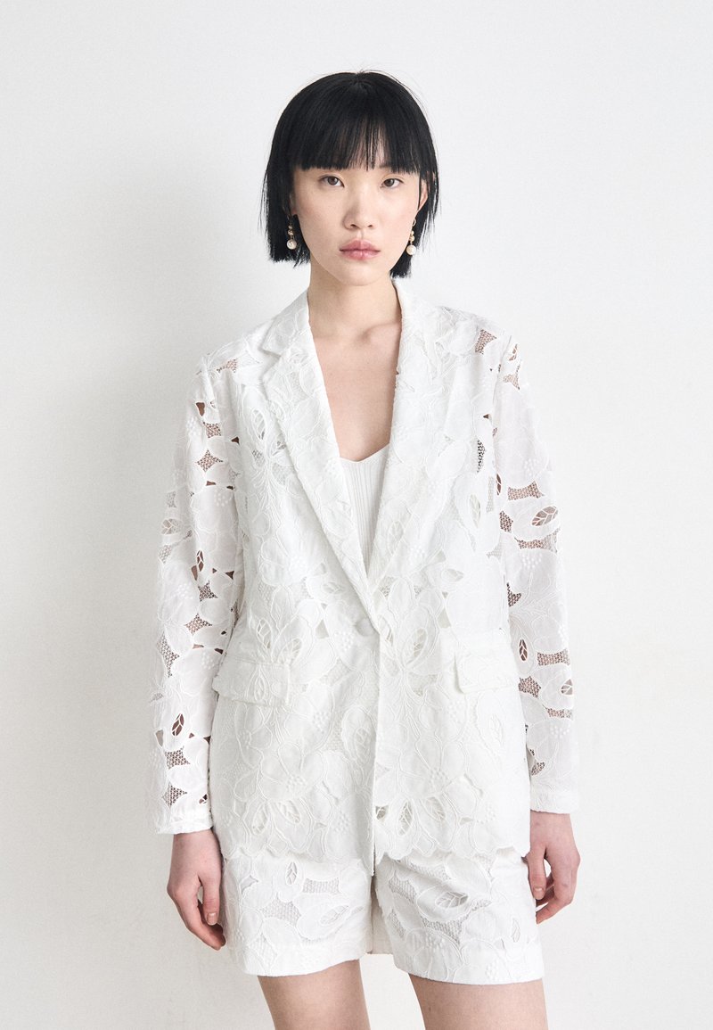 White lace blazer with floral patterns, featuring a single-button closure and two front pockets, paired with matching shorts.