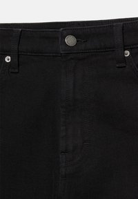 Gros plan de la taille d'un jean en denim noir avec un bouton argenté, des passants pour ceinture, des coutures de poche avant et des rivets sur un tissu foncé.