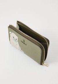 Green leather wallet featuring a bear illustration, a gold zipper, and a smooth texture. Logo embossed on the front. Two compartments visible.