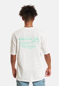 Weißes Baumwoll-T-Shirt mit kurzen Ärmeln, mit mintgrünem Text und Kaffee-Grafiken auf der Rückseite. Lässige Passform, weicher Stoff.