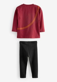 Chemise rouge en coton à manches longues avec un accent courbé marron ; associée à des leggings noirs, les deux présentant une texture lisse et un design simple.