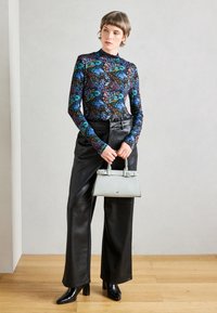 Langärmeliges Oberteil mit mehrfarbigem Blumenmuster, kombiniert mit hochtaillierten schwarzen Lederhosen und einer kleinen hellgrauen Handtasche. Schwarze Stiefel mit Absatz.