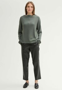Olijfgroen, langmouwtrui met hoge kraag; gecombineerd met slanke, zwarte leren broeken en zwarte instappers. Eenvoudige, relaxed fit.