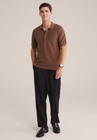 Hnědá pletená polo košile s texturovaným vzorem, tříknoflíkovou légou a krátkými rukávy. Spárována s černými volnými kalhotami a černými botami.