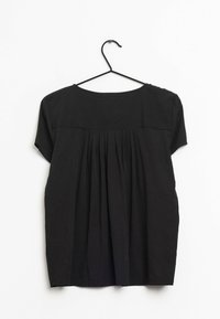 Blouse noire à manches courtes avec un design plissé à l'arrière et un col rond, présentée sur un cintre devant un fond blanc.