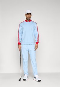 Light blue golf tracksuit with red accents, featuring a zip-up collar, long sleeves with stripes, and matching pants. White cap and shoes.