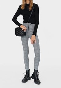 Czarna dopasowana bluzka z długim rękawem, szaro-czarne legginsy w kratkę z wysokim stanem oraz czarne lace-up bojówki. Czarna pikowana torba na ramię.