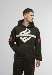 Fekete kapucnis pulóver piros díszítéssel, nagy fehér ROCAWEAR logóval, elülső zsebbel és a bal ujjon található "99" számmal. Puha anyag, lazán szabott fazon.
