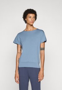 Blue short-sleeve top with a round neckline, soft texture, and a fitted elastic hem. Paired with navy pants featuring large pockets.