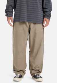 Baggy beige cargo pants with large back pockets, paired with a dark gray striped long-sleeve shirt and black canvas sneakers.