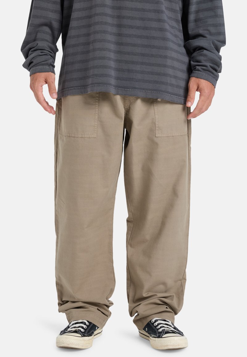 Baggy beige cargo pants with large back pockets, paired with a dark gray striped long-sleeve shirt and black canvas sneakers.