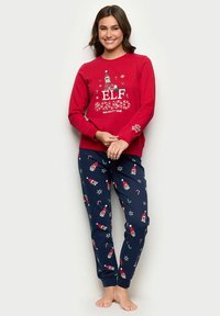 Punainen pitkähihainen paita, jossa on "ELF SQUAD" -grafiikka ja leikkisä joulutonttumuotoilu, yhdistettynä tummansinisiin housuihin, joissa on tonttu- ja karkkitankokuvioita. Puuvillasekoitetta.