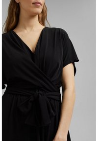 Robe noire enveloppante en tissu lisse, dotée d'un décolleté en V profond et de manches courtes, avec une ceinture nouée à la taille pour un ajustement réglable.