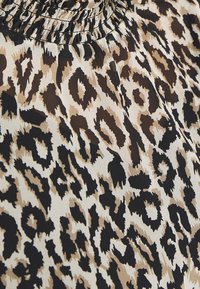 Gros plan sur un tissu avec un motif imprimé animalier marron, noir et beige et des fronces près du haut.