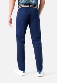 Marinblå bomullsbyxor med rak passform, som har bakfickor och ett vävt bälte i tan, kombinerat med vita sneakers.