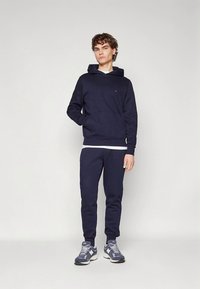 Bluza i spodnie dresowe w kolorze granatowym, wykonane z polaru. Bluza posiada kaptur, kieszeń z przodu oraz niewielkie logo na piersi.