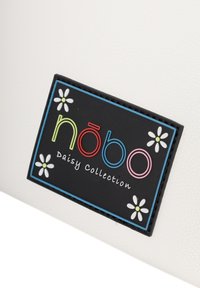 Valkoinen teksturoitu laukku, jossa on musta logopatchi värikkäillä kirjaimilla ja daisy-grafiikoilla, merkitty "nōbo Daisy Collection".