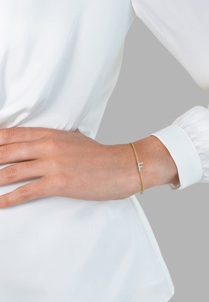 Gold chain bracelet with a delicate design, featuring a small decorative element and a smooth texture, worn on a wrist.