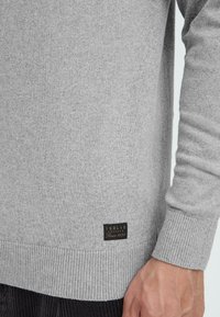 Gray sweater made of soft fabric; features ribbed cuffs and hem; includes a small black label with "SOLID" and "Since 1999" at the bottom.