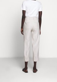 Ljusbeiga linbyxor med avslappnad passform, kort längd och två bakfickor. Bärs med en enkel vit t-shirt och platta sandaler.