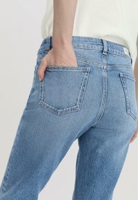 Jeans de mezclilla azul claro con corte ajustado, con una cintura de altura media, bolsillos traseros y una textura sutil.