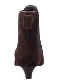Botín de ante marrón con un acento de cuero, que presenta un tacón curvado y paneles laterales elásticos para facilitar su uso. Textura suave.