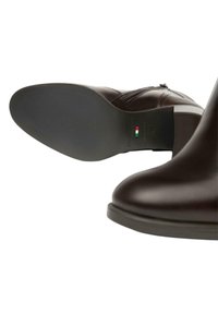 Stivale alla caviglia in pelle marrone con punta arrotondata, zip laterale e suola in gomma texturizzata. Presenta un tacco minimale e un dettaglio con la bandiera italiana.