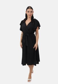 Vestido negro tipo envolvente con mangas cortas de volantes, cintura ceñida, falda fluida y detalle de lazo. Textura suave, diseño hasta la rodilla.