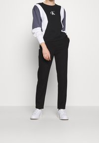 Sudadera bloqueada en negro y gris con detalles en blanco, que presenta un logo bordado. Combinada con pantalones negros ajustados y zapatillas blancas.