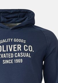 Navyblauwe hoodie met witte tekst "Quality Goods Oliver Co. Elevated Casual Since 1969" op de borst, toont bovenste torso en capuchon.