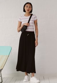 Stripet t-skjorte med korte ermer i rosa og hvite striper, sammen med et svart maxiskjørt og hvite sneakers; liten svart crossover-veske.