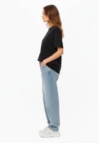 Maglietta nera a maniche corte abbinata a jeans a gamba dritta di colore blu chiaro e sneakers bianche. L'outfit presenta una vestibilità comoda e texture morbide.
