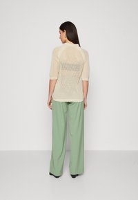 Beige gjennomsiktig strikket topp med trekvart ermer, kombinert med høyt liv lys grønne vide bukser. Svarte flate sko.