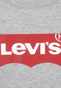 Šedá mikina s kulatým výstřihem, na které se nachází velké červené logo Levi's v bílé barvě, umístěné na texturovaném pozadí.