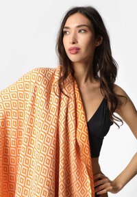 Orange mønstret sjal med et diamantdesign i hvid. Stoffet ser blødt ud med en let draperingseffekt, der er svøbt omkring skuldrene.