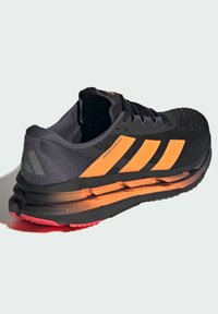 Black and orange running shoe featuring a textured upper, three bold stripes, padded heel, pronounced sole, and red outsole accents.