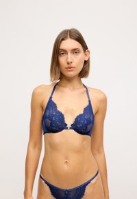 Reggiseno in pizzo blu navy e perizoma abbinato con scollatura profonda, spalline regolabili e dettaglio decorativo con chiusura frontale.