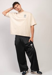 Beežist üle suurusega t-särk graafilise trükiga, mida kannavad lahtised mustad dressipüksid logoga. Tumesinised ja kreemjad tossud.