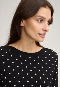 Μαύρο πουλόβερ με λευκές πουά, ριμπ λαιμόκοψη, μαλακή υφή και άνετη εφαρμογή. Το σχέδιο διαθέτει ομοιόμορφα τοποθετημένες πουά για κλασική εμφάνιση.