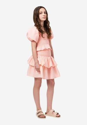 Sukienka z puff-sleeve w delikatnym różu, z falbaniastymi warstwami i marszczonym stanikiem. Połączona z jasnobeżowymi klapkami.