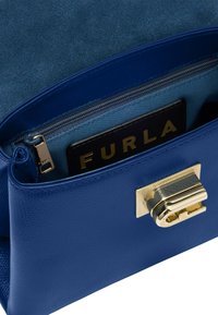 Blauwe leren handtas met een gestructureerde buitenkant, gouden accenten en een ritsvak. Het interieur toont een contrasterende blauwe voering en een merklabel.
