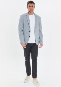 Jasnoszary blazer z dwoma guzikami, połączony z białym t-shirtem, czarnymi spodniami w kratę i beżowymi sneakersami. Gładki materiał i dopasowany krój.