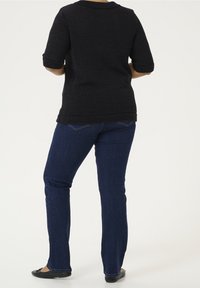 Czarny sweter z teksturą, z krótkimi podwiniętymi rękawami, zestawiony z ciemnoniebieskimi jeansami o prostych nogawkach oraz czarnymi płaskimi butami. Widok od tyłu.