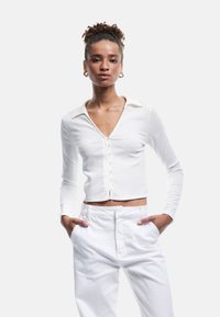 Witte geribbelde langesleeve crop top met een V-hals, knoopsluiting en kraag, gecombineerd met witte high-waisted broek.